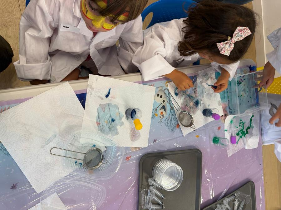 Dos niños con bata haciendo un experimento de color con pipetas